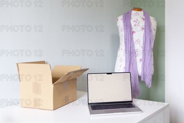A cozy workspace featuring a mannequin with a scarf, a laptop, and a shipping box, symbolizing the process of organizing a closet to sell clothing online