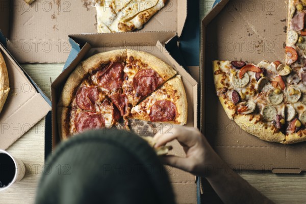 Cropped unrecognizable person taking a slice of pepperoni pizza from a box, accompanied by friends at a casual gathering