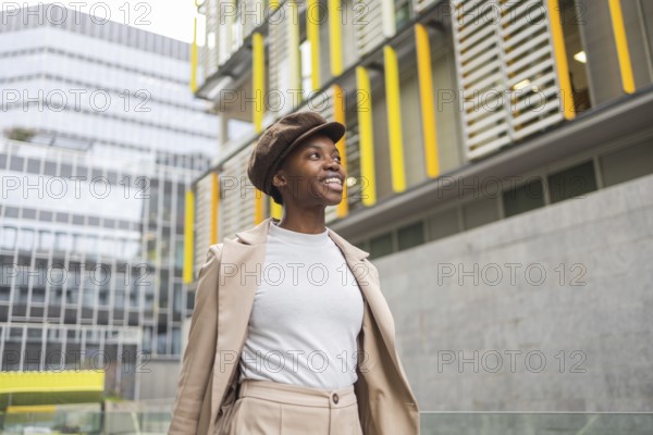 A fashionable black woman walks through an urban area, surrounded by contemporary architecture Her confident smile complements the city's vibrant atmosphere