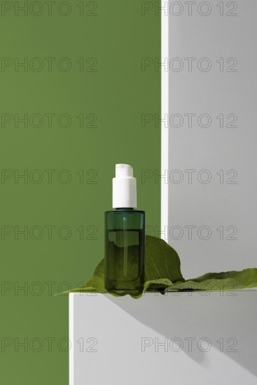 Close-up view of a green glass essential oil bottle placed on a white stand with a large green leaf, set against a vibrant green background. The natural setting emphasizes the product's use in skincare and wellness