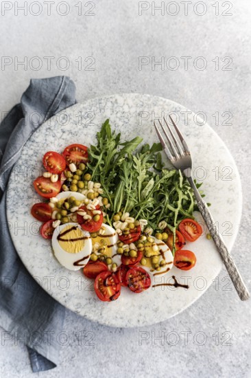 A vibrant keto salad featuring boiled eggs, rocket, cherry tomatoes, green peas, and sprouted beans, elegantly topped with balsamic sauce for a nutritious touch