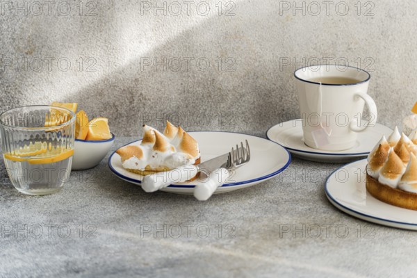 An elegant table setting with lemon meringue tarts, a cup of tea, and fresh lemon slices. Ideal for a cozy afternoon tea or brunch ambiance