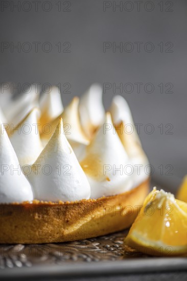 Close up of a a homemade lemon cake showcasing the golden brown peaks of toasted meringue. The dessert rests on a decorative plate with fresh lemon wedges nearby