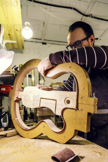 A skilled luthier at work in a workshop, carefully crafting a bass guitar using specialized tools and techniques. Warm lighting highlights the artisan's dedication and precision