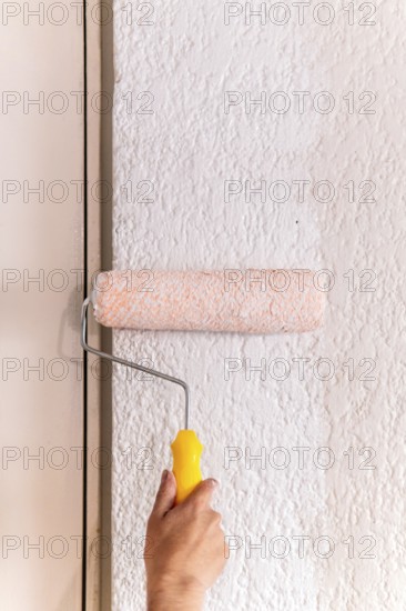 Cropped unrecognizable of a man's hand using a paint roller on a textured wall, capturing a moment of home remodeling