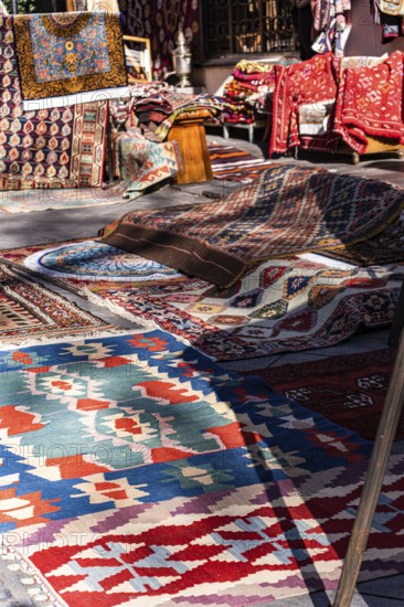 A vibrant collection of traditional Georgian rugs and textiles displayed in an outdoor market in Tbilisi, Georgia. The intricate patterns and bold colors showcase the region's rich cultural heritage