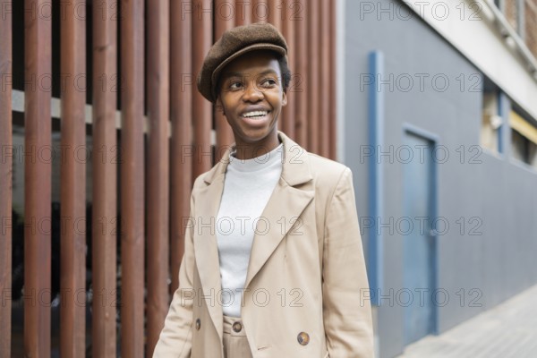 A black woman in an urban environment, wearing a stylish beige outfit paired with a beret She smiles confidently, reflecting modern city fashion trends