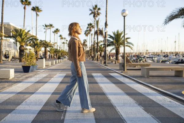 A Mixed-race woman walks along a marina promenade bordered by palm trees at sunset The relaxed atmosphere and scenic views create a sense of tranquility and leisure