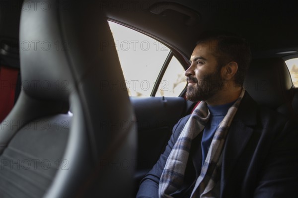 Indian male businessman dressed in formal wear with a winter scarf, traveling in the backseat of a car, looking out the window