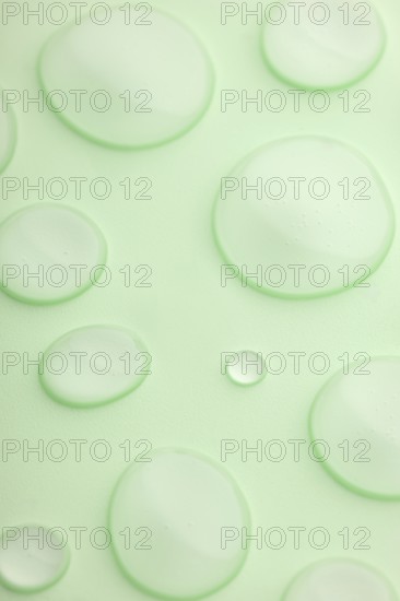 This image features a close-up view of translucent droplets scattered on a smooth, light green surface The droplets vary in size, creating a fresh and calming atmosphere