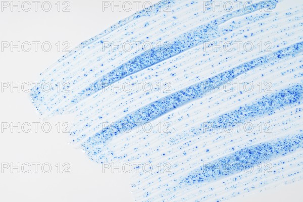 A close-up of face scrub smears showcases fine blue micro-exfoliating particles against a smooth white background, emphasizing skincare and cleansing texture