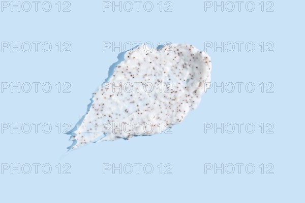 Exfoliating cream with microbeads smeared against a pale blue background, showcasing the texture for beauty and skincare products