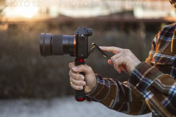 Close-up of hands holding a camera and adjusting the screen during golden hour The scene captures the soft lighting of the sunset, highlighting the camera's details
