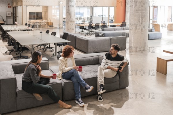 Three coworkers engage in a friendly and productive discussion in a modern office lounge, highlighting teamwork and collaboration Bright, open space fosters creativity