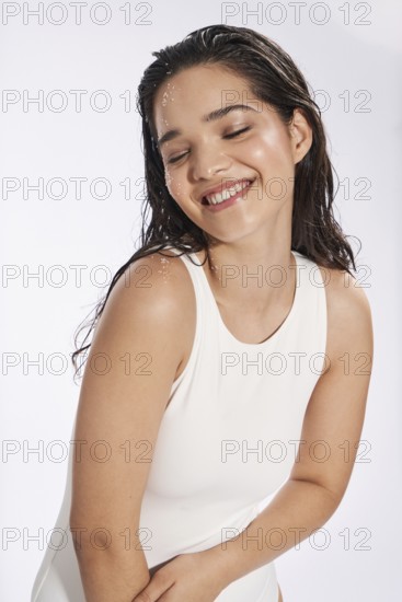 Fresh model portrait of a delighted woman, with eyes closed with a subtle smile, styled in a white sleeveless top, adorned with delicate glitter. Captured beautifully in a studio environment