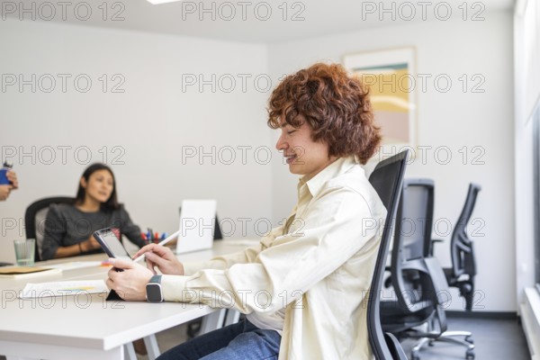 A team of coworkers collaborating in a bright, modern office One person is focused on a tablet, while another listens intently, fostering a productive environment