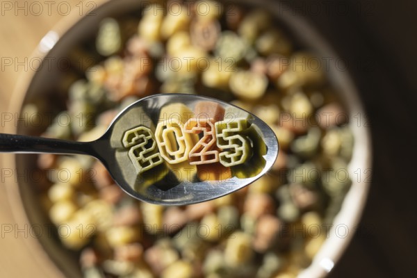 A spoonful of numerically shaped pasta displays the year 2025 above a bowl full of colorful number pasta, symbolizing new year celebrations