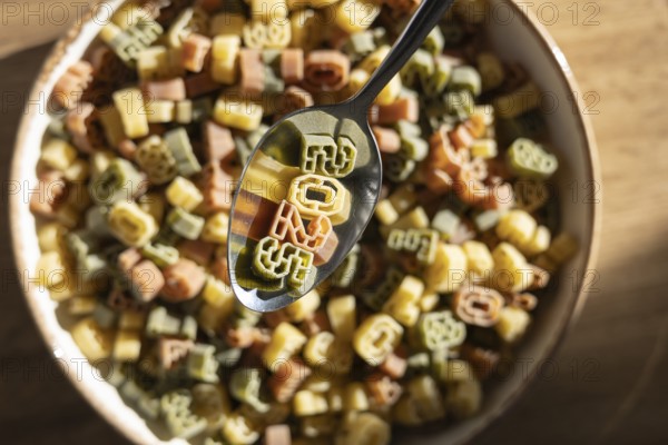 Top view of a metal spoon lifting colorful number shaped pasta from a bowl, clearly showing the numbers 2025, symbolizing the new year, amidst a variety of other numerals