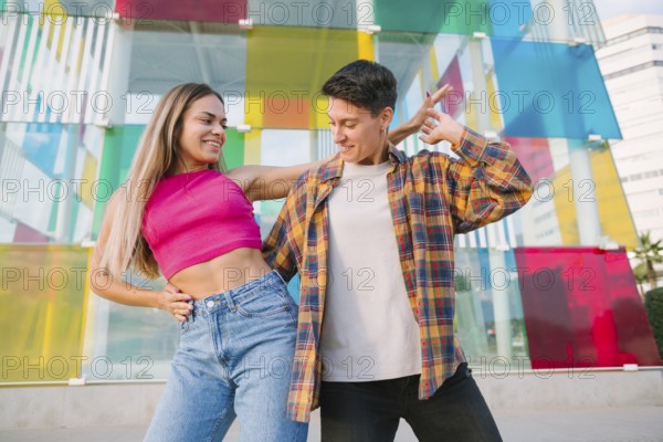 A joyful lesbian couple shares a playful dance, smiling and enjoying the moment. The vibrant glass wall behind them adds an artistic and dynamic touch, symbolizing love, fun, and self-expression