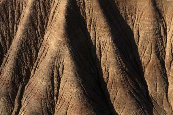 Aerial view of a rugged desert landscape showcasing intricate erosion patterns and ridges in brown tones, capturing the stark beauty of arid terrain and natural formations