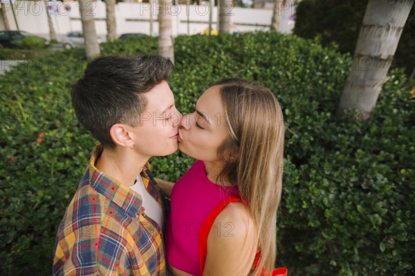 Happy lesbian couple sharing a kiss in a lush outdoor setting, celebrating love and diversity. Embracing pride, inclusion, and the joy of a genuine connection