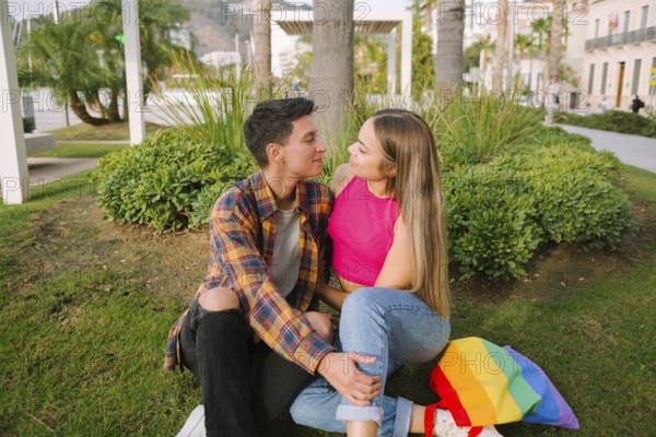 A joyful lesbian couple sits in a park, sharing a loving gaze. With a rainbow flag backpack beside them, they celebrate love and pride in an inclusive and diverse setting