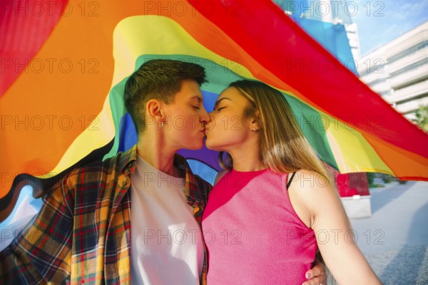 A joyful lesbian couple shares a tender moment under a vibrant rainbow flag, symbolizing pride and love. Celebrate diversity and inclusivity with this heartwarming image