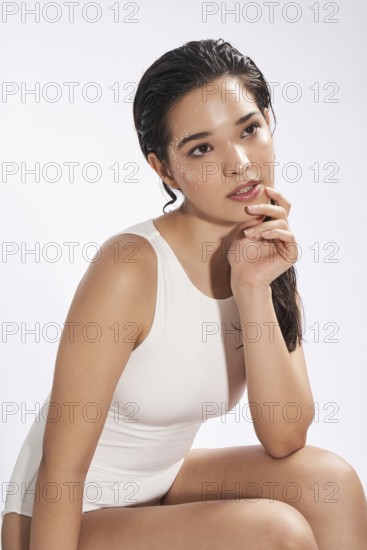 A fresh portrait of a young woman wearing a white bodysuit in a studio setting, gazing slightly away from the camera with a thoughtful expression and wet hair adorned with shimmery flakes