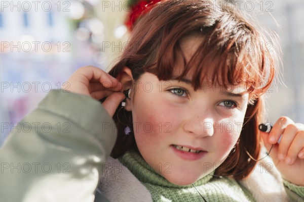 A girl with auburn hair adjusts her earbud while seated on a bus, showcasing a moment of technology use during travel