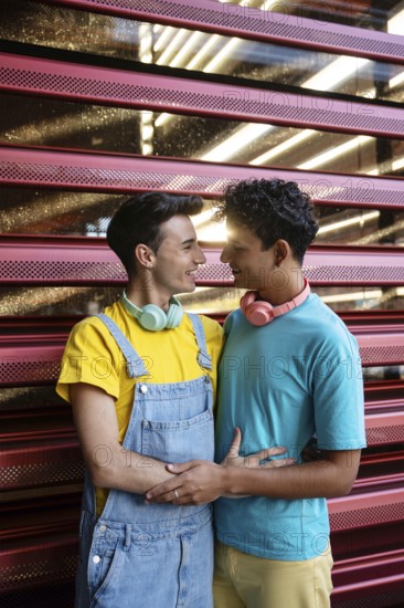 A joyful couple, wearing colorful casual outfits, share a loving moment. They look at each other with smiles, standing against a modern exterior. The scene radiates love