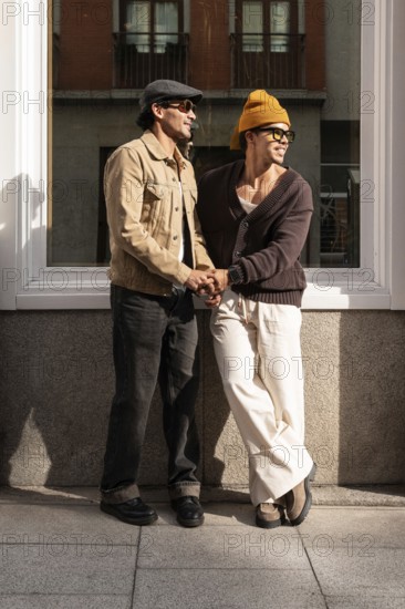 A Colombian couple stand outside in the city, sharing a moment of laughter. Dressed casually, they both wear sunglasses and smile warmly as sunlight casts gentle shadows