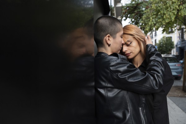 A loving lesbian couple shares an intimate, tender moment while standing closely against a wall in an urban street, showcasing their connection and affection for one another