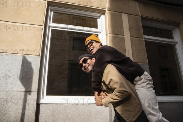 A happy gay couple in stylish attire celebrates love on a sunny day. The urban backdrop highlights their joyful connection and playful energy, capturing a candid moment of togetherness
