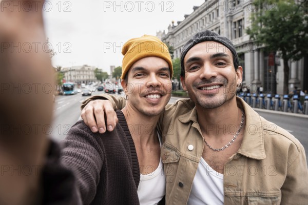 A Colombian gay couple smiling while taking a selfie outdoors, capturing an authentic, joyful moment on a busy city street. They appear relaxed and happy, enjoying their day