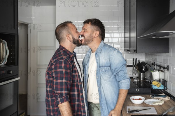 A joyful gay couple in a kitchen, playfully sharing cream from a dessert, showcasing love and happiness in a cozy home setting
