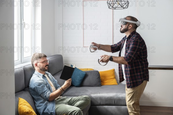 A gay couple engages in leisure activities in their living room. One reads a book while the other immerses in virtual reality gaming, creating a cozy and relaxed atmosphere