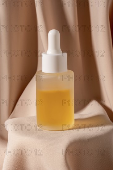 A minimalist flat lay photo featuring a glass dropper bottle of golden skincare The bottle is elegantly placed on soft peach fabric, creating a spa-like atmosphere