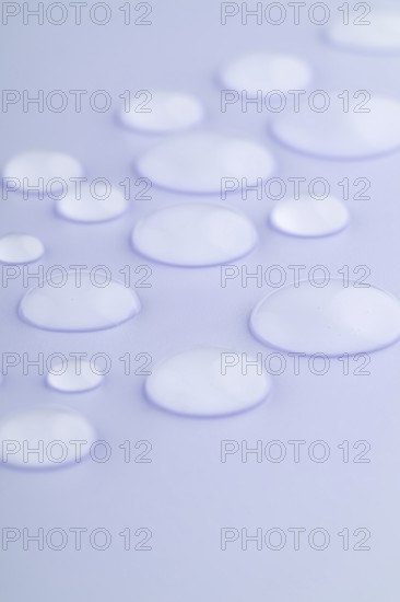 Close-up image of droplets scattered on a smooth, lavender-colored surface The droplets vary in size, creating a calming and serene visual effect