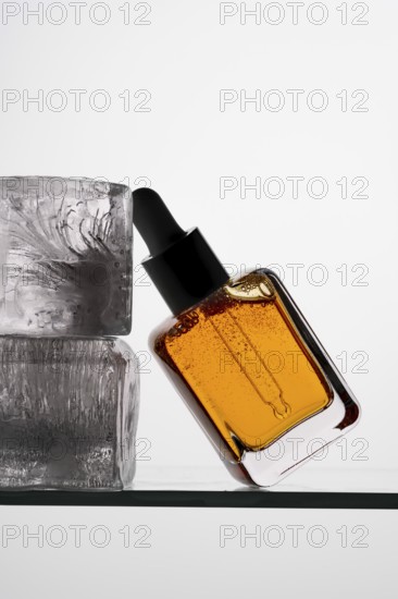 Aesthetic close-up of a vitamin C serum in a clear pipette bottle resting against ice blocks on a glass surface Perfect for skincare and wellness themes