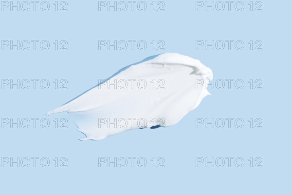 Smooth texture of a white cream or gel smear, isolated on a serene blue background, representing skincare and beauty products