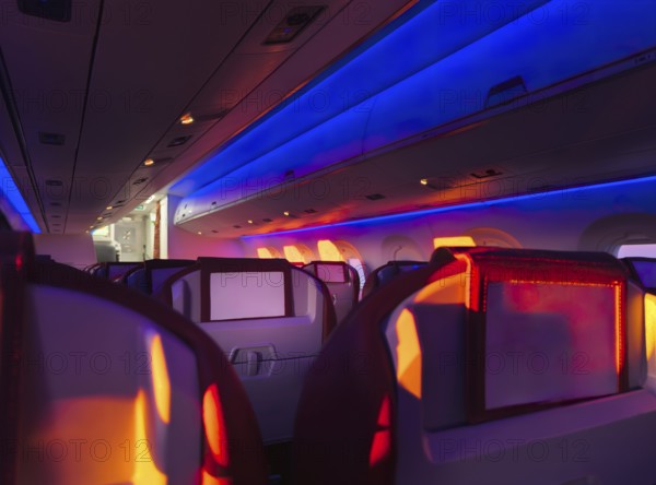 Interior view of an airplane cabin aglow with vibrant mood lighting, showcasing the comfortable seating and modern ambiance during a nighttime flight
