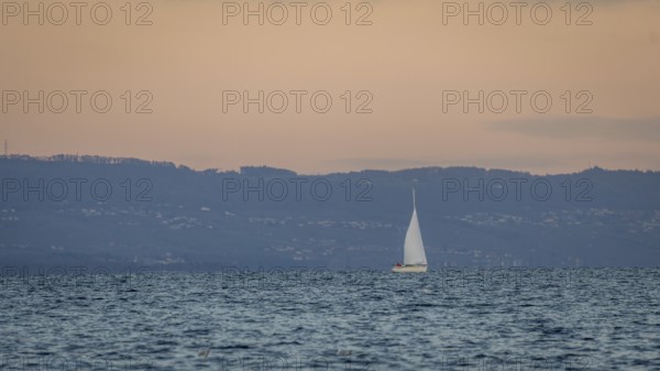 A serene scene of a sailboat gracefully moving across a calm lake in Geneva, set against a backdrop of distant hills during a tranquil sunset, creating a peaceful atmosphere