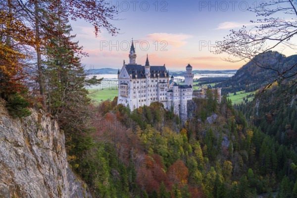 Nestled in the Bavarian Alps, Neuschwanstein Castle stands majestically amidst vibrant autumn foliage The fairytale architecture overlooks lush valleys and distant landscapes, captivating visitors