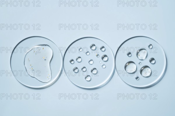 Three transparent petri dishes with water droplets placed on a light blue surface The circular arrangements create a minimalist and scientific aesthetic