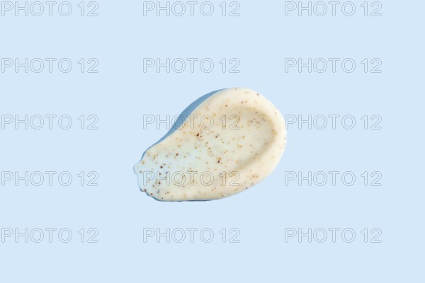 A dab of exfoliating cream with visible scrub particles smeared on a pastel blue background showcasing the texture of skincare products