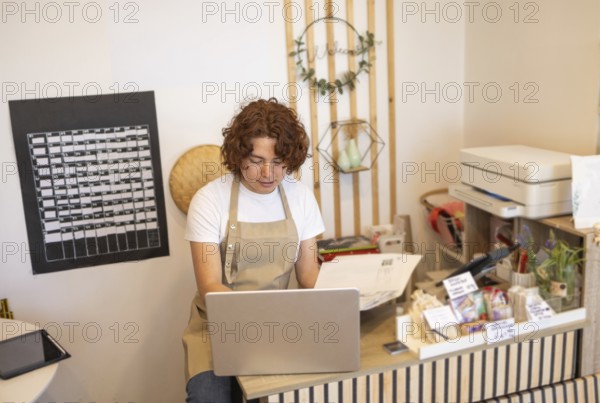 A young shop assistant in an apron uses a laptop at the counter of an organic store The workspace is surrounded by eco-friendly products and minimalistic, natural decor