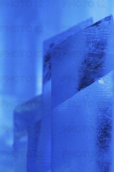 Close-up of intricately shaped ice structures illuminated with a cool blue glow at a temporary ice hotel in Swedish Lapland, capturing the serene beauty of winter artistry