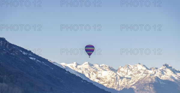 A vibrant hot air balloon floats gracefully over the Swiss Alps, showcasing a panorama of snow-clad peaks in a serene daytime scene. The clear sky enhances the tranquil beauty