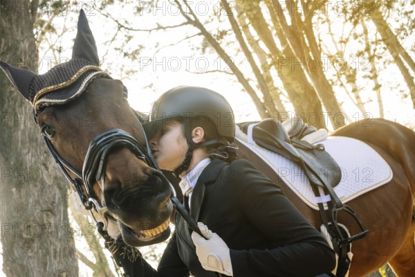 A teenage girl in classical dressage attire gently embraces her horse in a peaceful forest setting, exemplifying the close bond between horse and rider