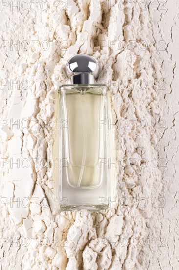 A sleek male perfume bottle rests on a cracked white sand texture, highlighting sophistication and luxury The minimalist design complements the natural, earthy backdrop